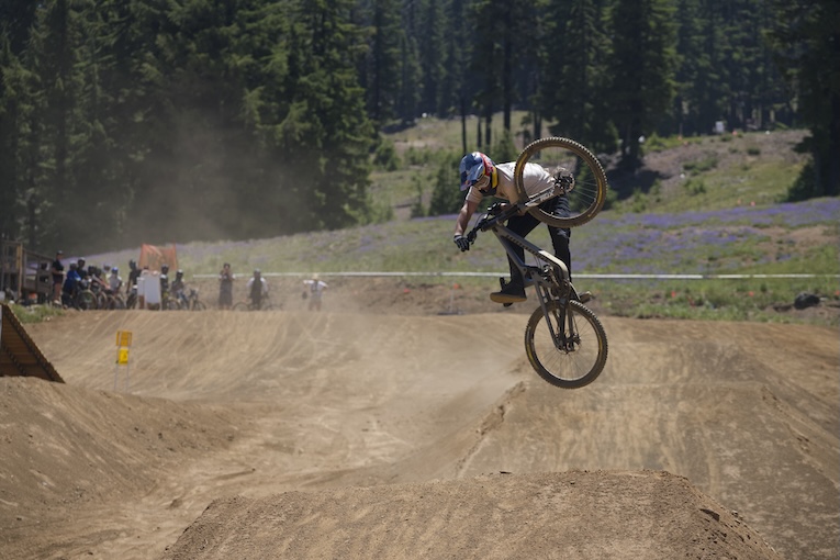 A mountain biker jumps off a middle jump in a dirt triple line.