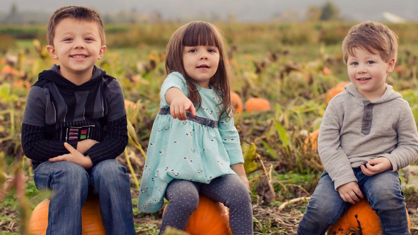 Children sitting on pumpkins.