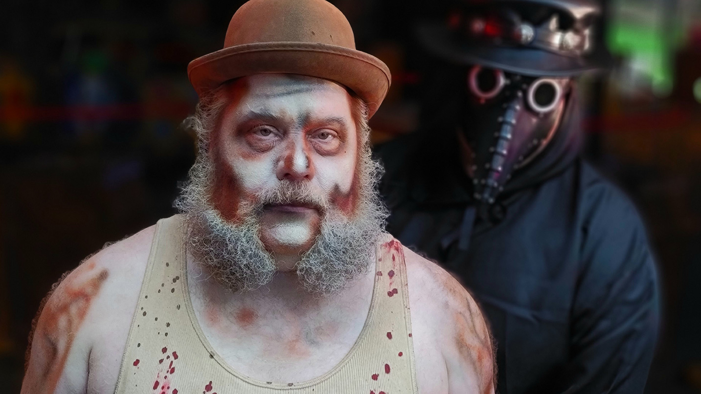 An adult man with costume makeup, fake blood splattered shirt and bowler hat. Behind him, another adult with a steampunk, bird-beak plague mask.