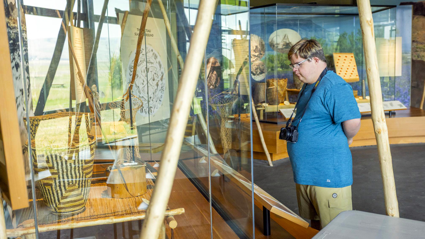 A young man views Native American items on display in a museum exhibit.