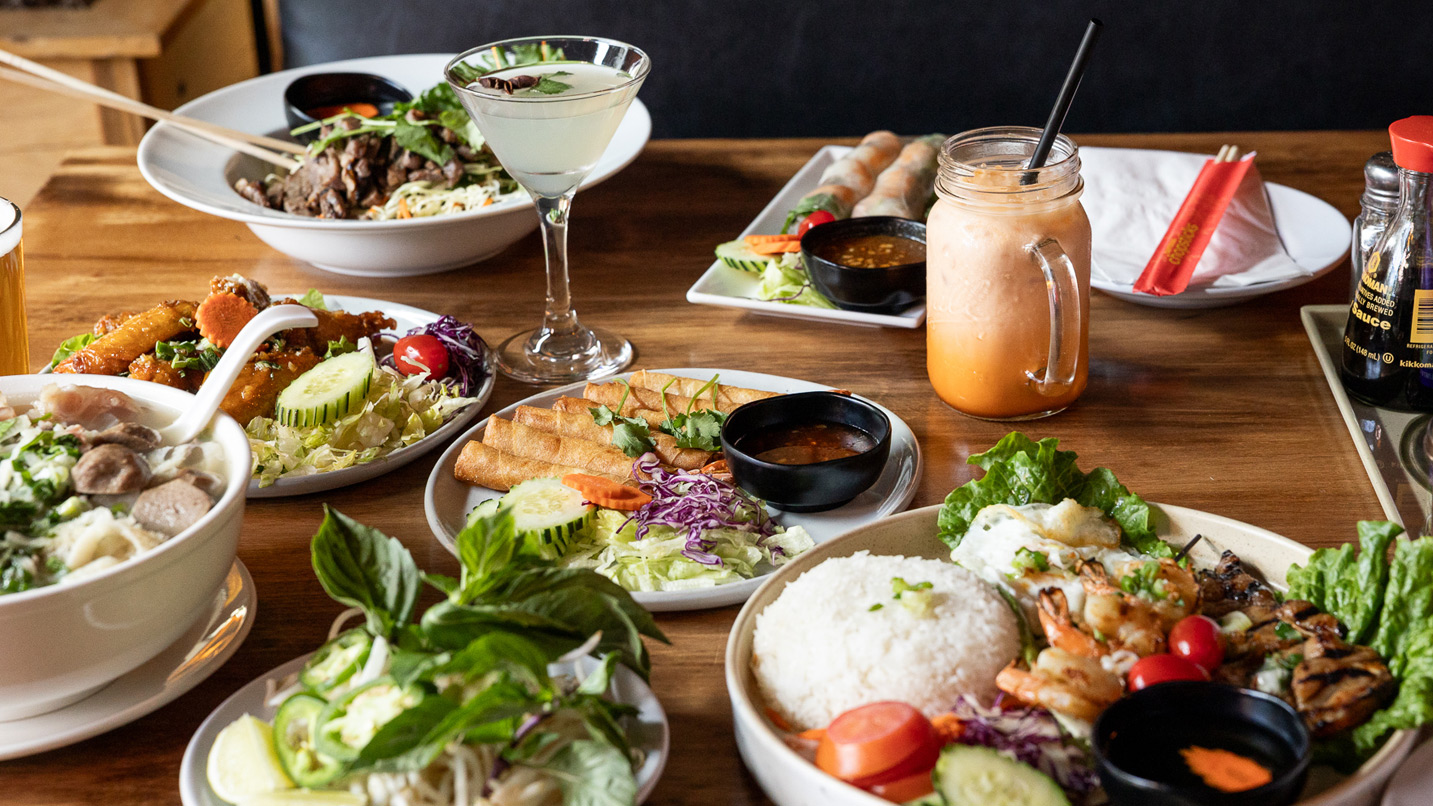Several dishes of traditional Vietnamese and southeast Asian food, including pho, fried spring rolls, Thai iced tea and rice bowls.