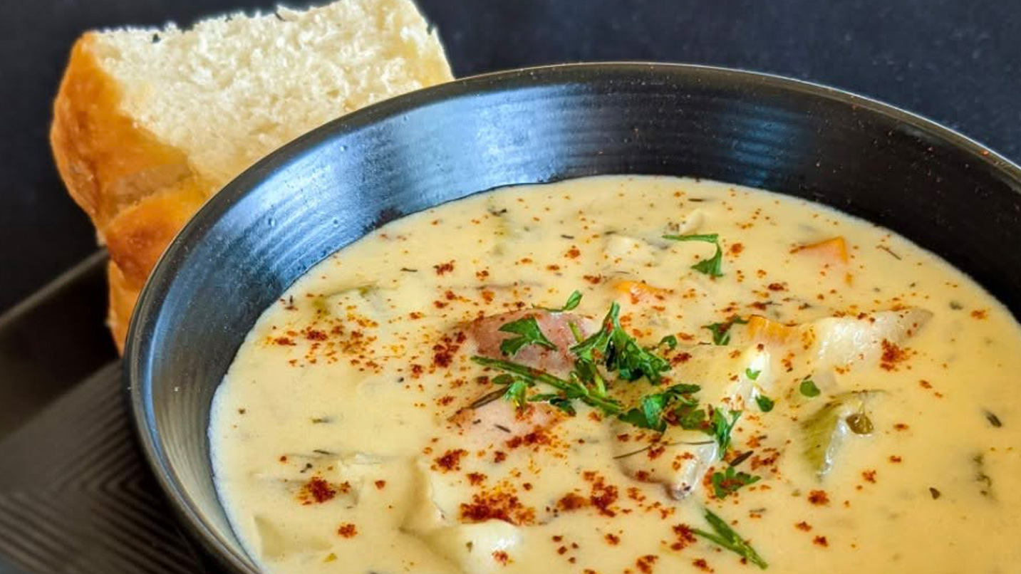 A bowl of clam chowder and a piece of bread.