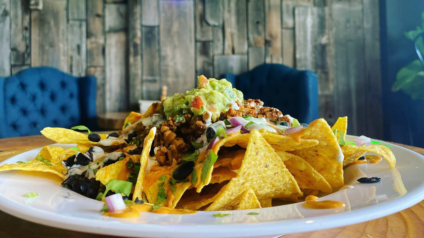 A plate of nachos topped with vegan meat, beans, onion, lettuce and guacamole.