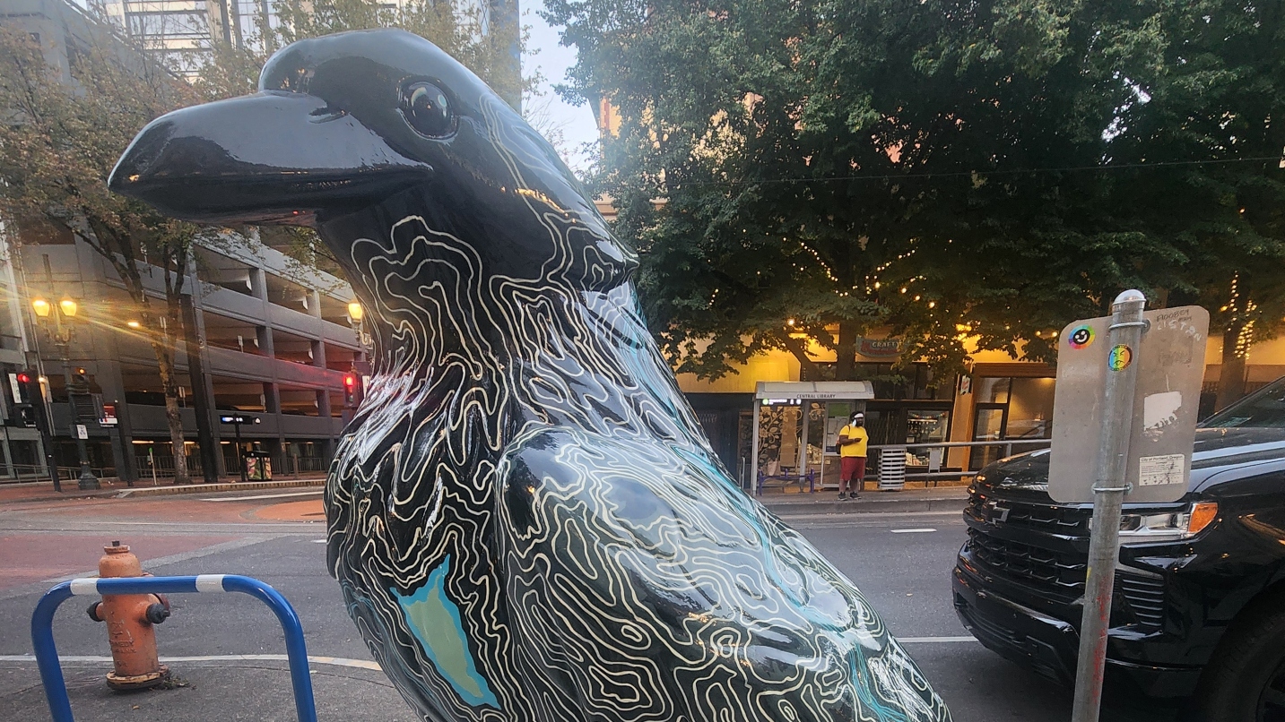Giant crow sculpture on a downtown street painted black with white curved lines.