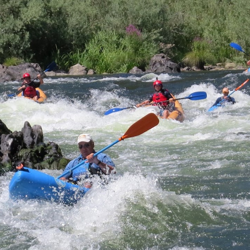 Several people paddle whitewater rafts down a river 