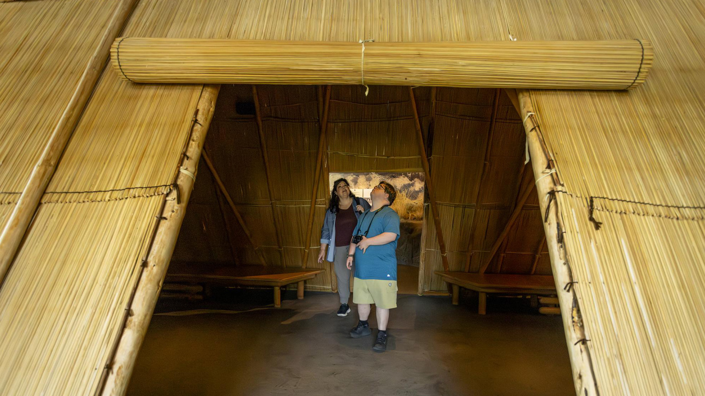 Two people in an indoor replica of a Native American straw hut at the Tamástslikt Cultural Institute.