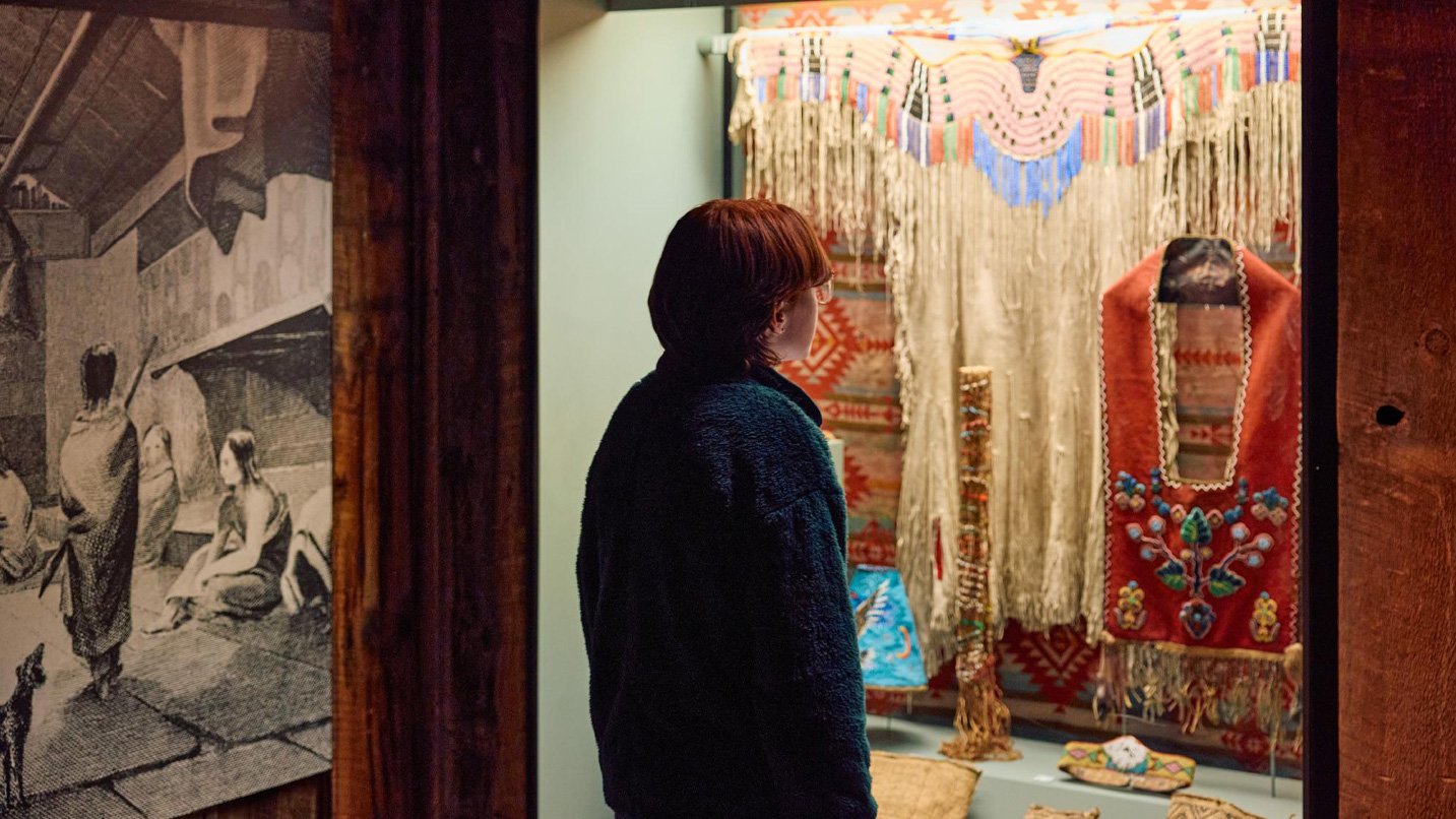 A young person looking at Native American clothing artifacts behind a glass exhibit.